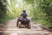 Person driving an ATV on a gravel road through a wooded area